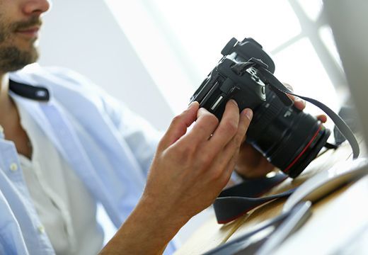 Ein junger Mann hält eine hochwertige Kamera in seiner Hand.